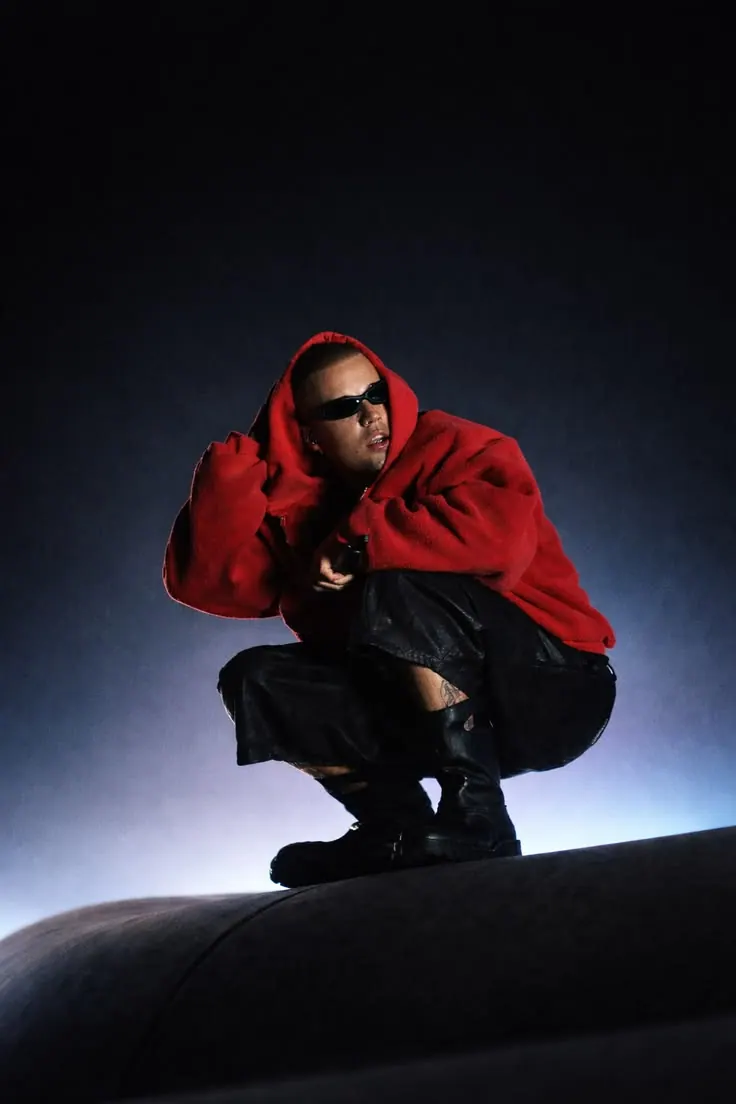 A red hoodie crouching on a tyre in the dark — men's portrait