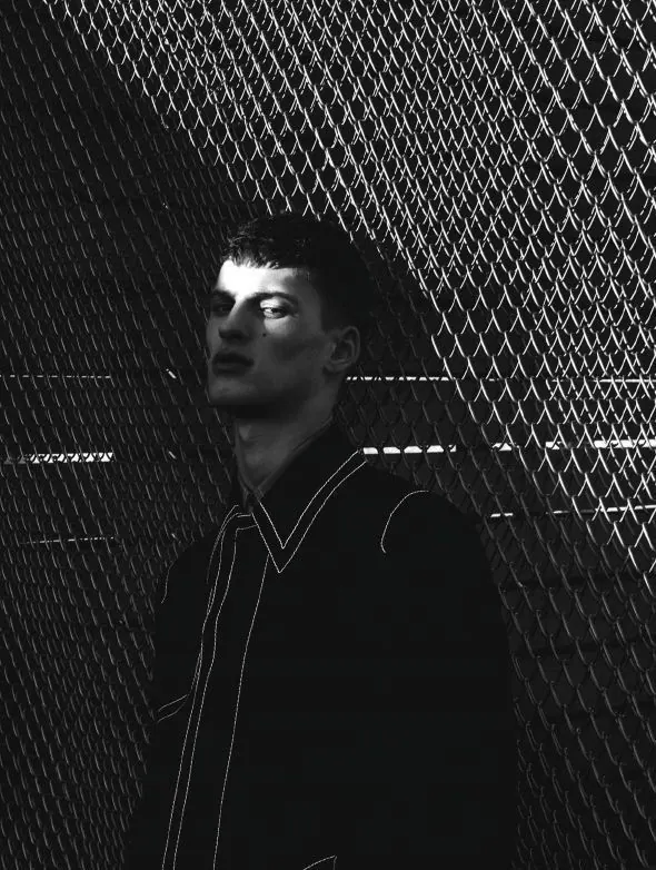 A monochrome male portrait beside a wire fence