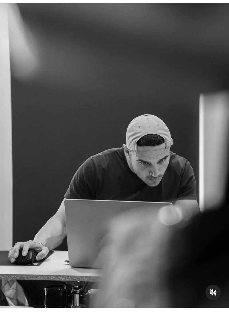 A baseball cap and laptop in a monochrome office — men's portrait