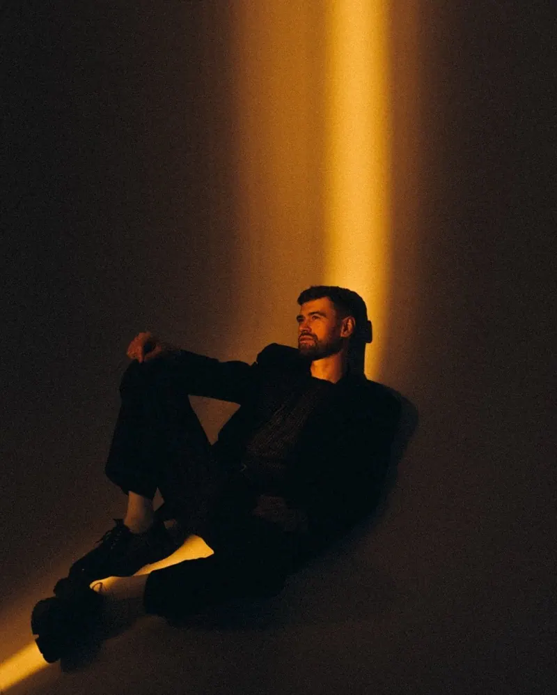 A black suit under a narrow amber spotlight — men's portrait