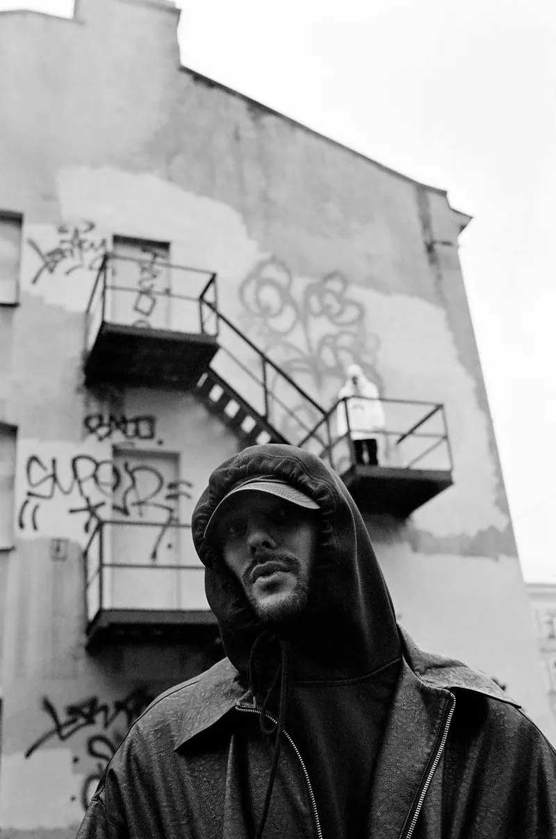 A cap beneath a fire escape in black and white — men's portrait