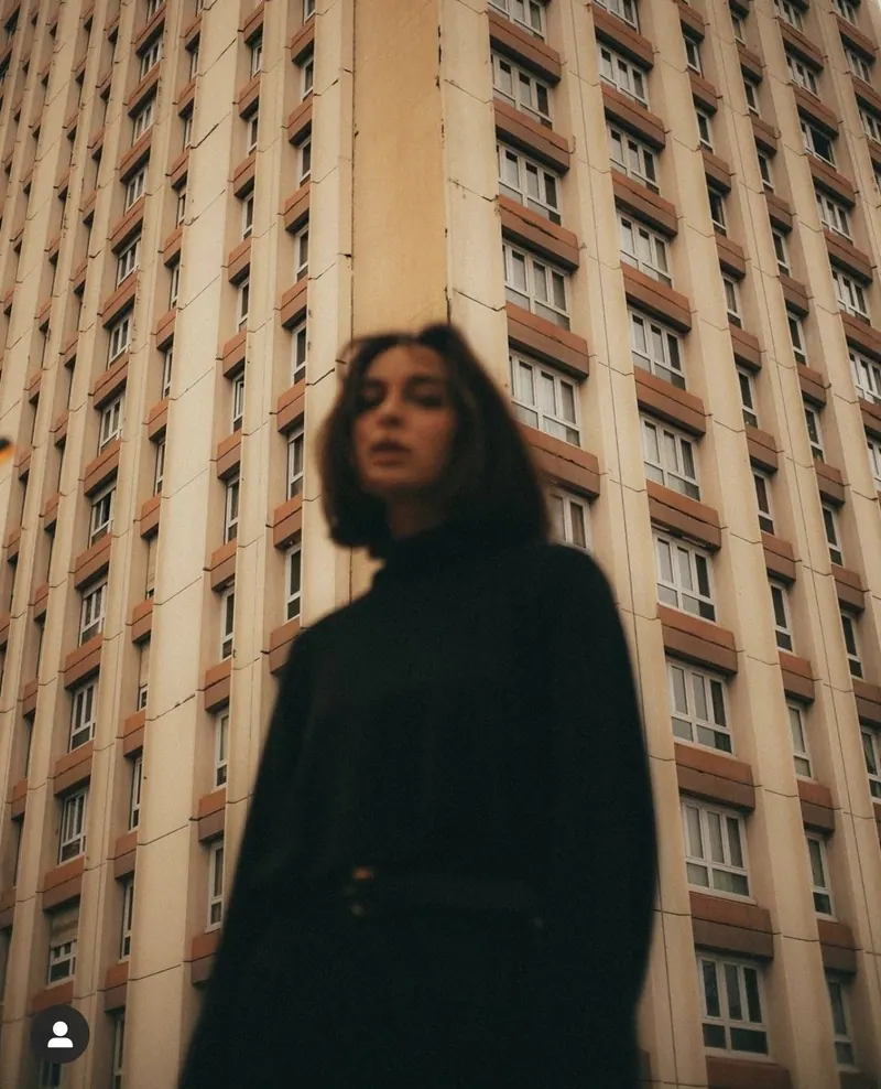 An all-black look beneath a tall city building — women's portrait